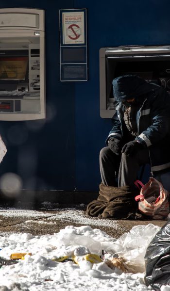 A homeless man is seen next to an outdoor ATM machine of a bank on Journal Square in Jersey City after a winter storm. (Reena Rose Sibayan | Jersey Journal file photo)